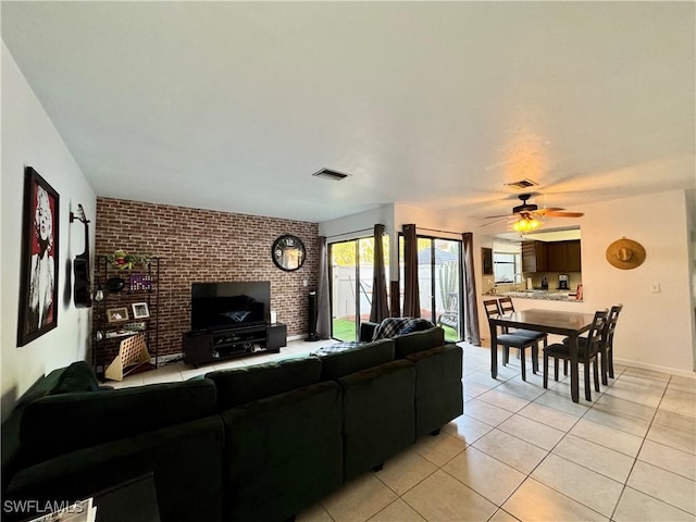 living room with light tile patterned flooring, ceiling fan, visible vents, and brick wall