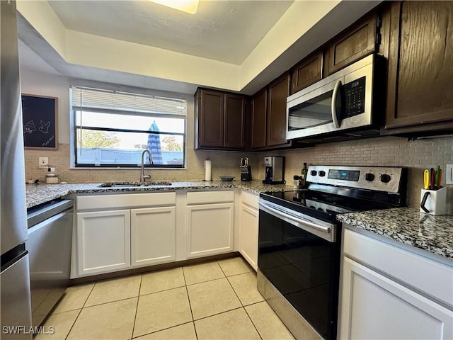 kitchen featuring light tile patterned floors, light stone counters, a sink, appliances with stainless steel finishes, and backsplash