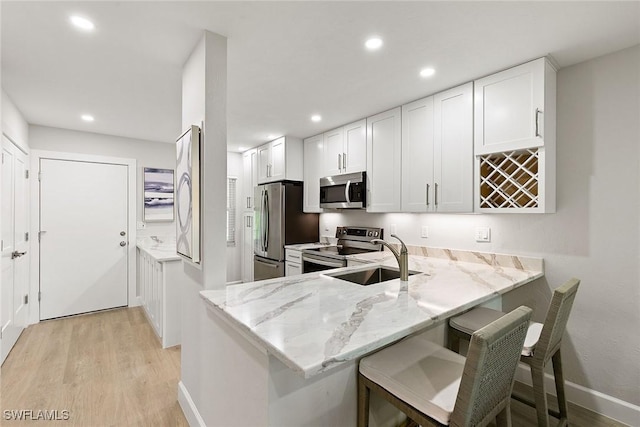 261 S Collier Blvd Unit 304, Marco Island, FL 34145 - kitchen featuring light wood-type flooring, white cabinetry, light stone counters, a sink, and stainless steel appliances