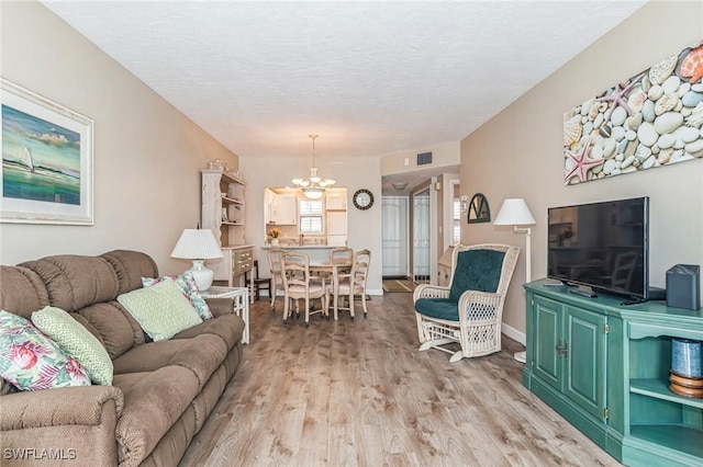 living area featuring a textured ceiling, baseboards, visible vents, light wood-style flooring, and a notable chandelier