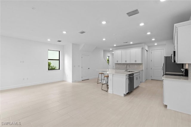 kitchen with stainless steel appliances, a breakfast bar area, a sink, backsplash, and white cabinets