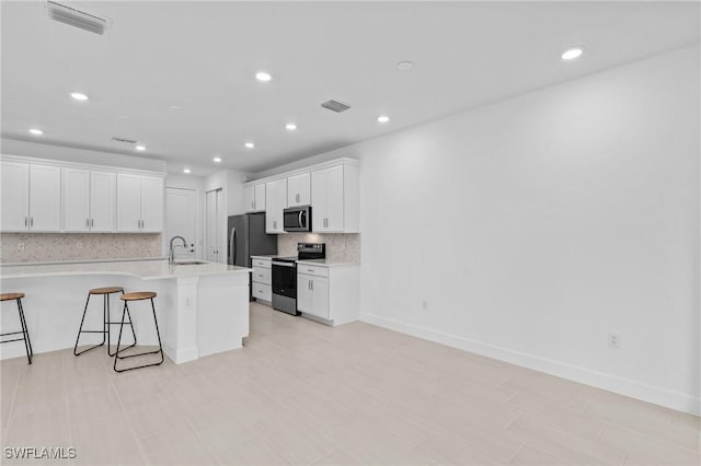 kitchen with stainless steel appliances, a kitchen bar, a sink, decorative backsplash, and white cabinetry