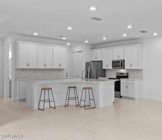 kitchen featuring appliances with stainless steel finishes, a kitchen island with sink, backsplash, white cabinetry, and a kitchen breakfast bar