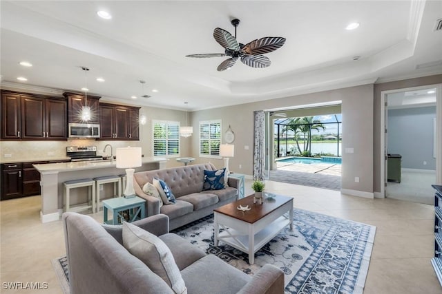 living area with a ceiling fan, recessed lighting, ornamental molding, light tile patterned floors, and a tray ceiling