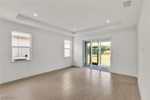 unfurnished room featuring a tray ceiling, visible vents, baseboards, and recessed lighting