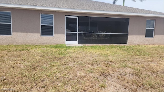 rear view of house featuring a lawn, stucco siding, and a sunroom