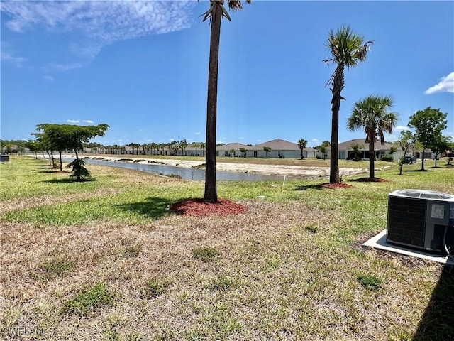 view of grassy yard with central AC and a water view