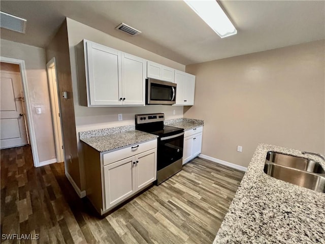 kitchen featuring stainless steel appliances, baseboards, a sink, wood finished floors, and white cabinetry