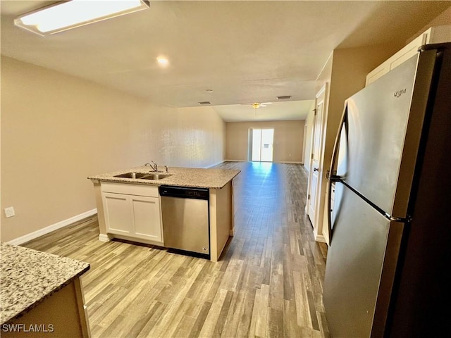 kitchen featuring stainless steel appliances, light wood-style floors, white cabinets, baseboards, and a sink