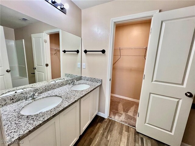 bathroom featuring wood finished floors, double vanity, baseboards, a shower, and a walk in closet
