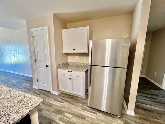 kitchen featuring freestanding refrigerator, wood finished floors, white cabinets, light stone counters, and baseboards