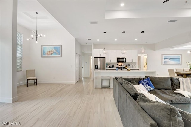 living room featuring a raised ceiling, recessed lighting, baseboards, light wood-type flooring, and a chandelier