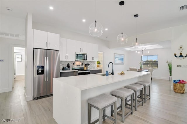 kitchen with stainless steel appliances, a sink, a kitchen breakfast bar, white cabinetry, and light wood finished floors