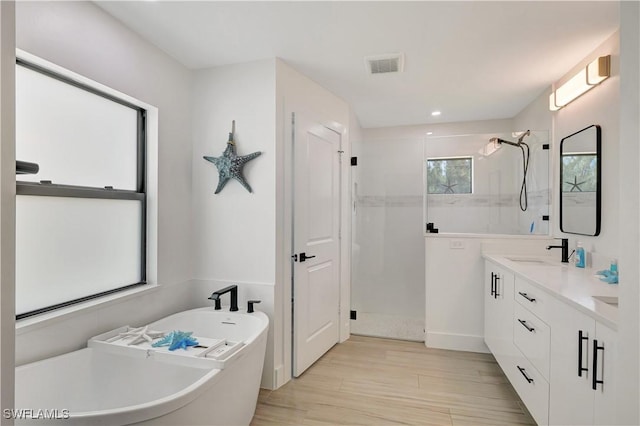 bathroom featuring a shower stall, a freestanding tub, wood finished floors, double vanity, and recessed lighting