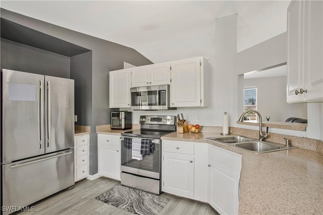 kitchen featuring stainless steel appliances, a sink, lofted ceiling, white cabinetry, and light wood finished floors