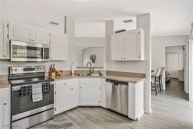 kitchen with appliances with stainless steel finishes, a sink, light wood-type flooring, and white cabinets