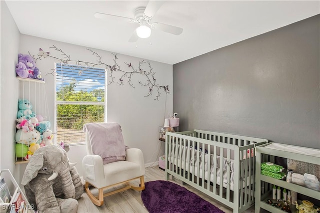 bedroom with wood finished floors, a nursery area, and ceiling fan