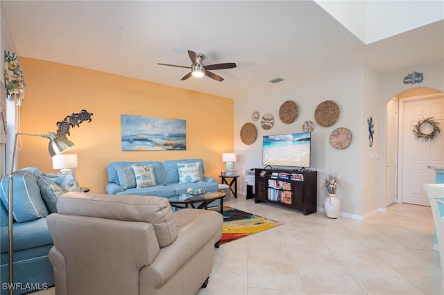 living room featuring visible vents, a ceiling fan, baseboards, arched walkways, and light tile patterned floors