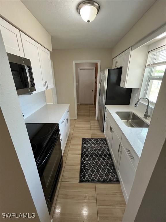 508 Wyoming Rd, Lehigh Acres, FL 33936 - kitchen with a sink, black electric range, stainless steel microwave, and white cabinetry