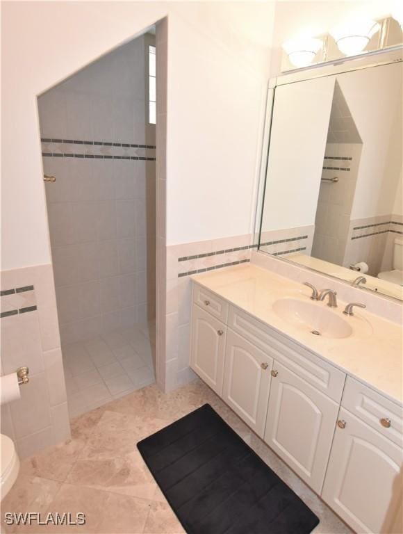 3787 Whippoorwill Ct, Punta Gorda, FL 33950 - bathroom featuring tile walls, wainscoting, a tile shower, vanity, and toilet