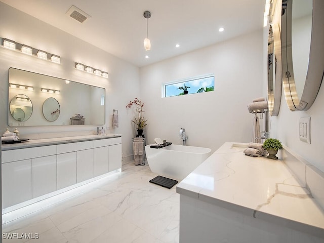 bathroom featuring visible vents, marble finish floor, recessed lighting, a freestanding bath, and two vanities