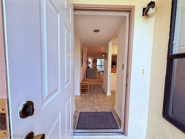 corridor featuring baseboards and a textured wall