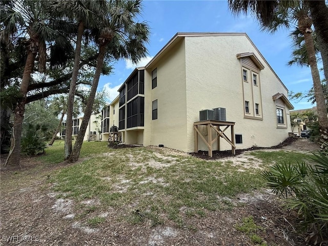 view of side of property featuring central air condition unit, stucco siding, and a lawn