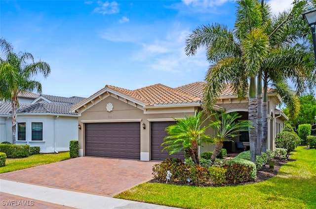 mediterranean / spanish-style house with a tiled roof, decorative driveway, a front lawn, an attached garage, and stucco siding