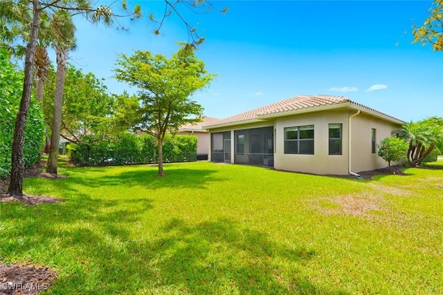 back of house with a lawn, a tiled roof, a sunroom, and stucco siding