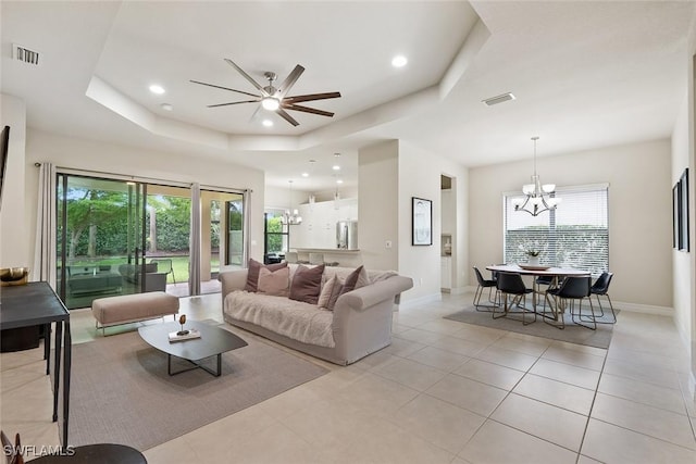 living area featuring ceiling fan with notable chandelier, light tile patterned floors, a tray ceiling, and visible vents