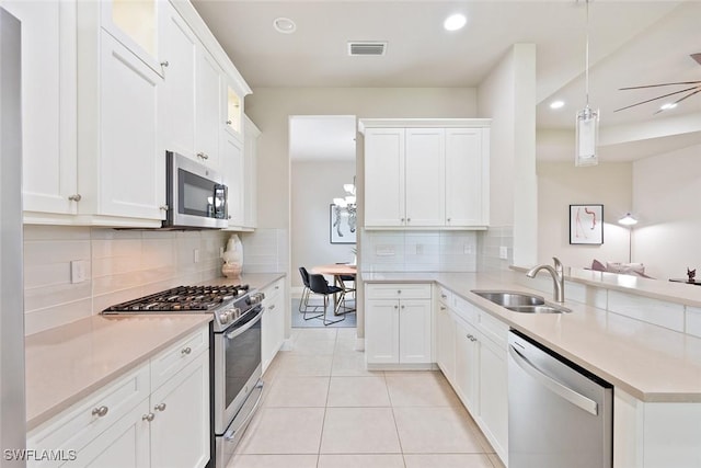 kitchen featuring light tile patterned flooring, a sink, stainless steel appliances, a peninsula, and decorative backsplash