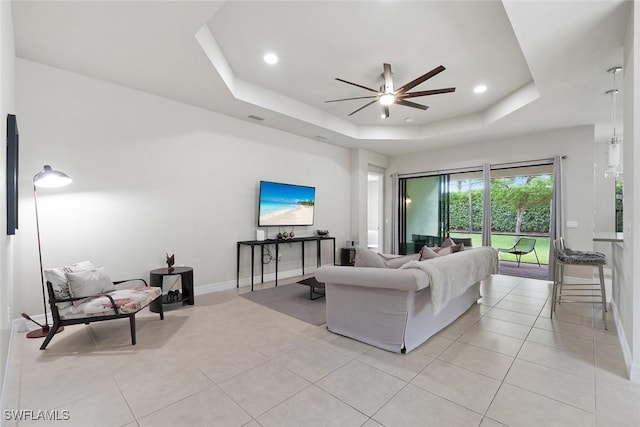 living room with a ceiling fan, baseboards, light tile patterned floors, a tray ceiling, and visible vents