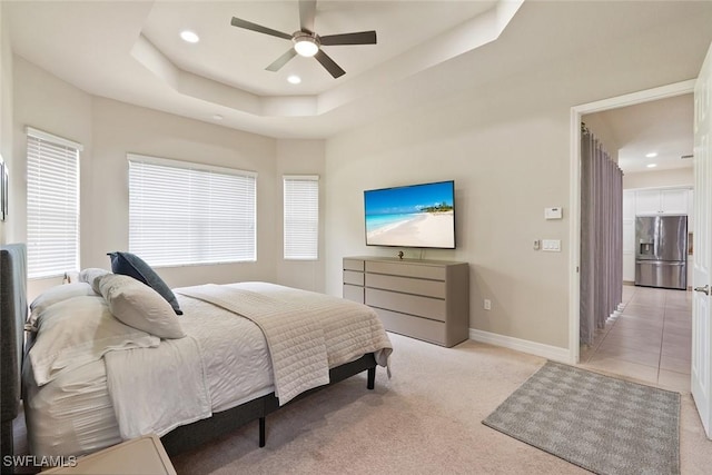 bedroom with light colored carpet, baseboards, stainless steel fridge, a tray ceiling, and recessed lighting