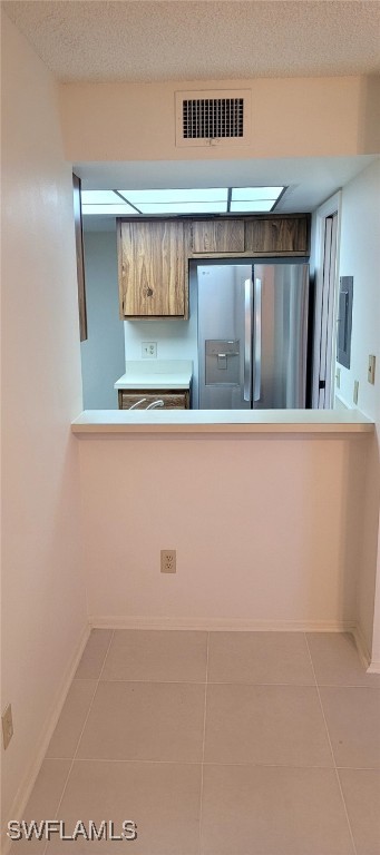 kitchen with stainless steel fridge, tile patterned flooring, a textured ceiling, baseboards, and visible vents