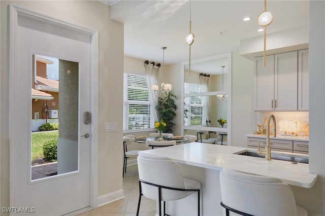 kitchen with a sink, light tile patterned floors, light stone countertops, and a kitchen bar