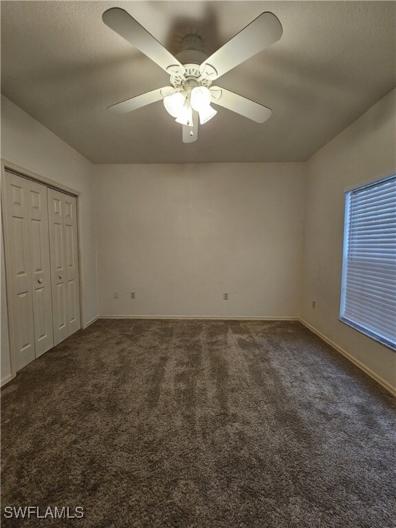 6025 Chardonnay Ln Unit 102, Naples, FL 34119 - unfurnished bedroom featuring dark colored carpet, baseboards, a closet, and ceiling fan