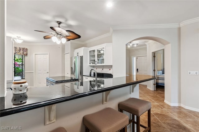 kitchen with dark countertops, ceiling fan, a kitchen bar, stainless steel refrigerator with ice dispenser, and arched walkways