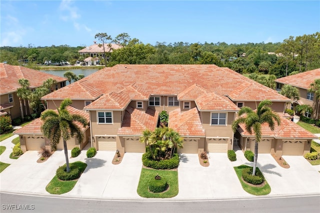 mediterranean / spanish house featuring a tiled roof, a water view, driveway, and a garage