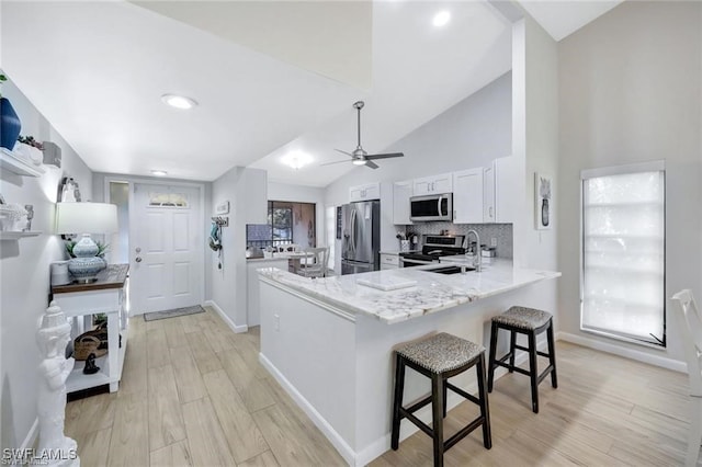 kitchen with a sink, light stone counters, a peninsula, a breakfast bar, and stainless steel appliances