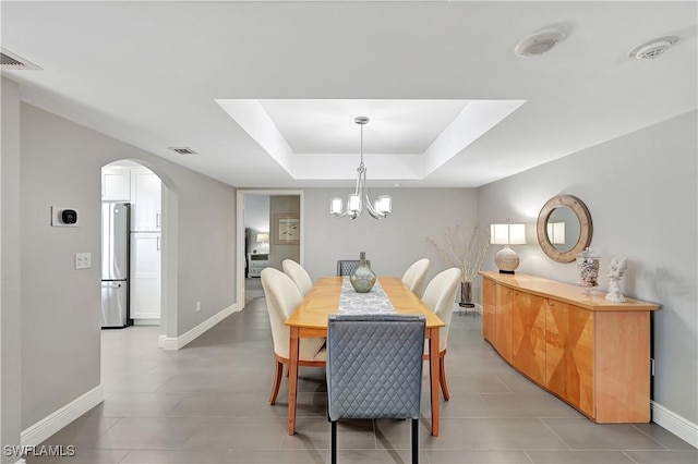 dining space with light tile patterned flooring, a raised ceiling, arched walkways, baseboards, and visible vents