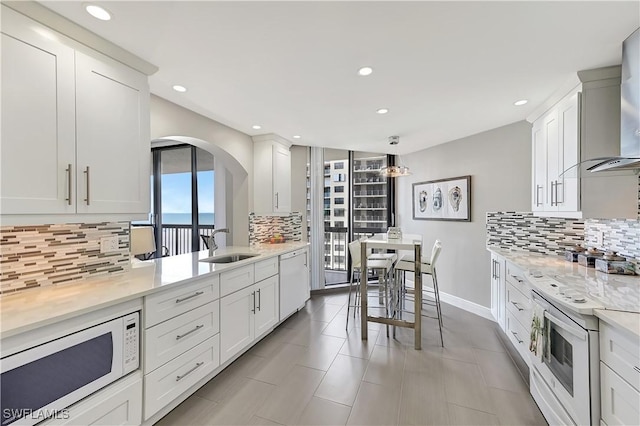 kitchen featuring arched walkways, tasteful backsplash, a sink, recessed lighting, and white appliances