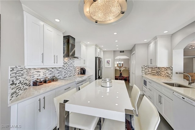 kitchen featuring wall chimney range hood, arched walkways, a sink, and dishwasher