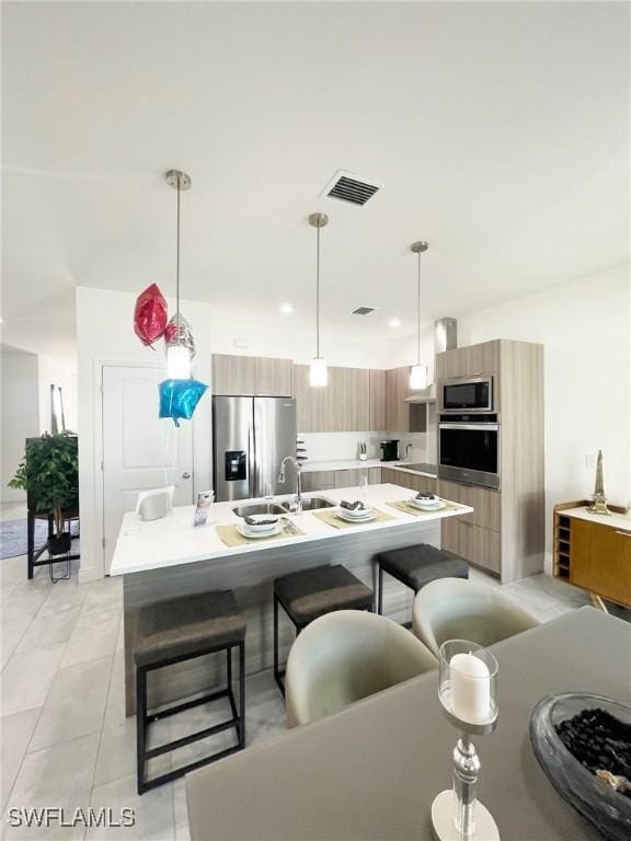 kitchen featuring a breakfast bar, stainless steel appliances, visible vents, a center island with sink, and modern cabinets