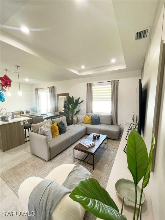 living room with a raised ceiling, recessed lighting, and visible vents