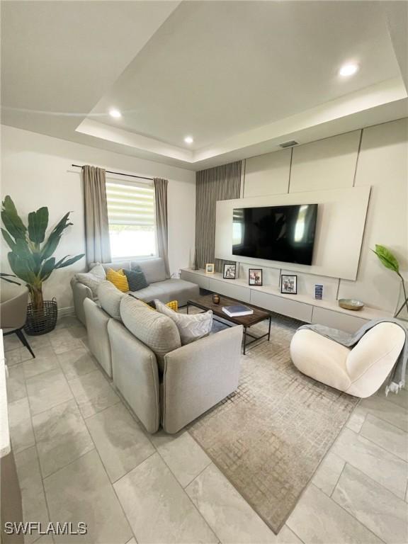 living area featuring a tray ceiling, recessed lighting, and marble finish floor
