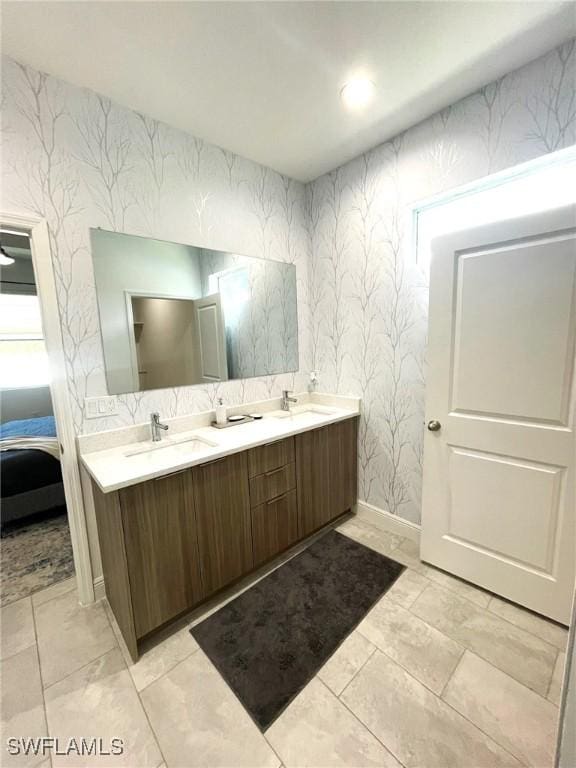 bathroom with double vanity, baseboards, wallpapered walls, connected bathroom, and a sink