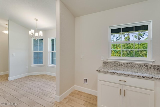 interior space with light stone countertops, baseboards, wood finish floors, white cabinets, and a chandelier