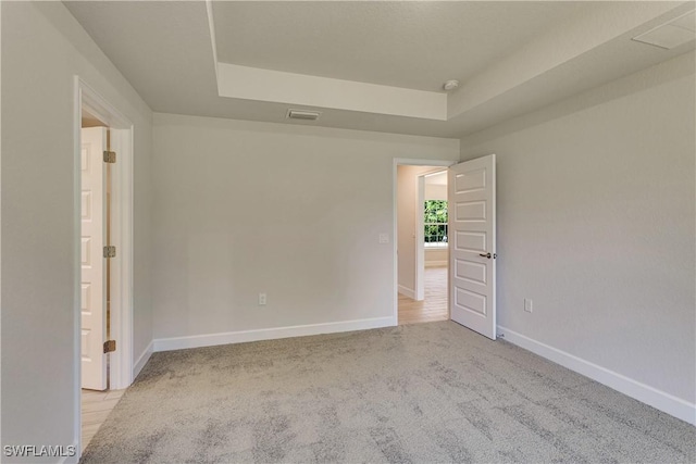 carpeted empty room with visible vents, baseboards, and a tray ceiling