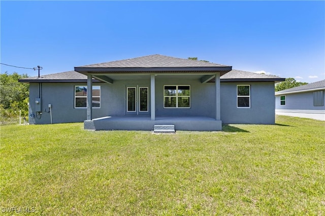 rear view of property featuring a yard, a patio, a shingled roof, and stucco siding