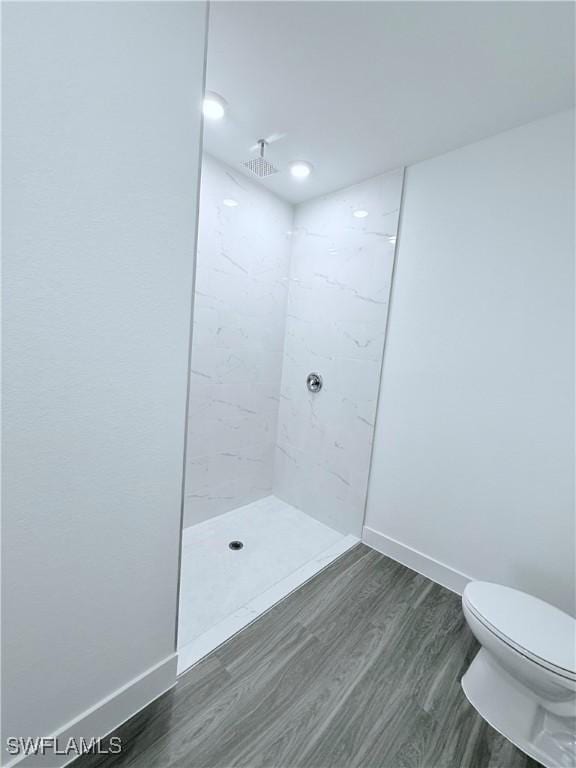 bathroom featuring baseboards, wood finished floors, toilet, and tiled shower